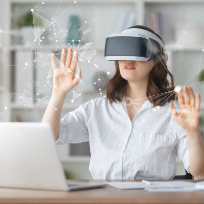 Metaverse technology concept. Woman with VR virtual reality goggles is working in the office. Futuristic lifestyle.